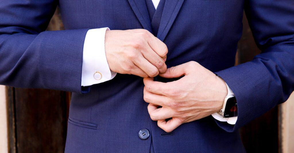 Close-up of a man's hands fastening a navy suit button, showcasing elegance and style.
