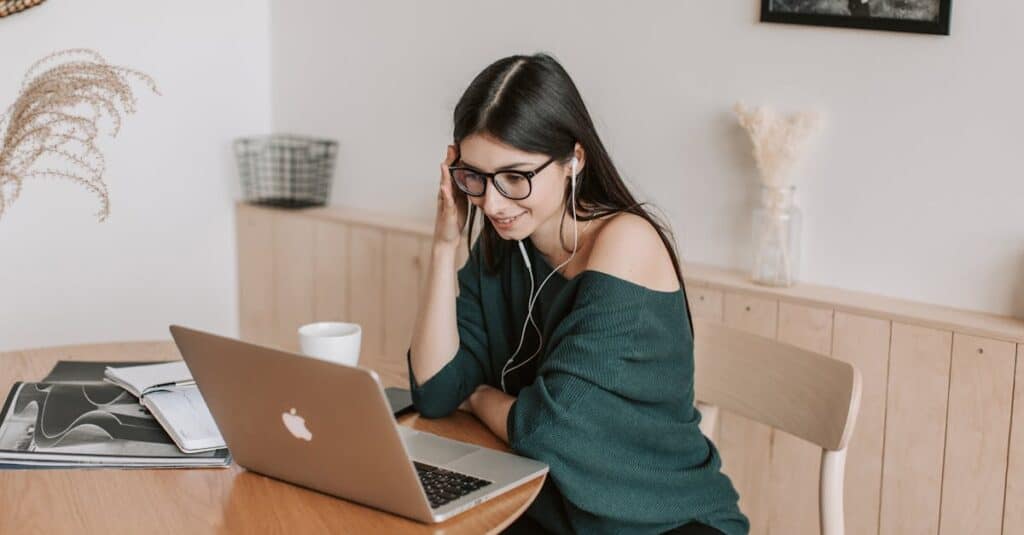 Smiling woman using laptop and earbuds for online learning in a cozy home setting.