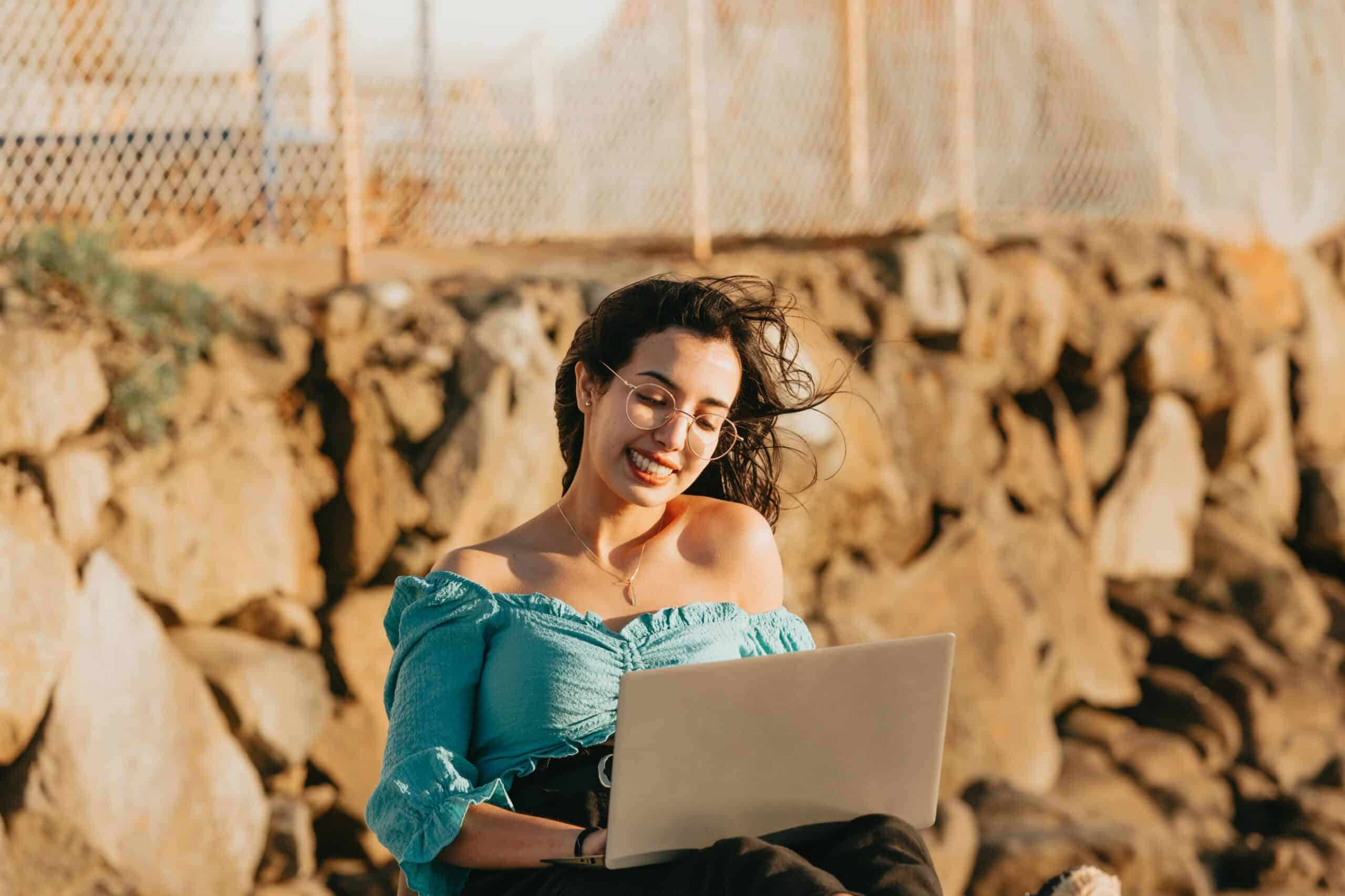 Woman enjoying remote work with laptop outdoors, smiling on a windy day.