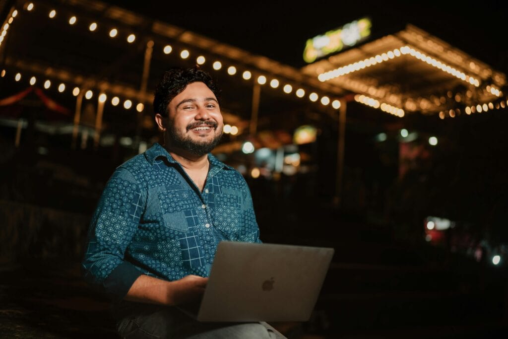 pexels-photo-19929601-19929601 Side Hustles in India. Cheerful man using laptop outdoors at night under festive lights.