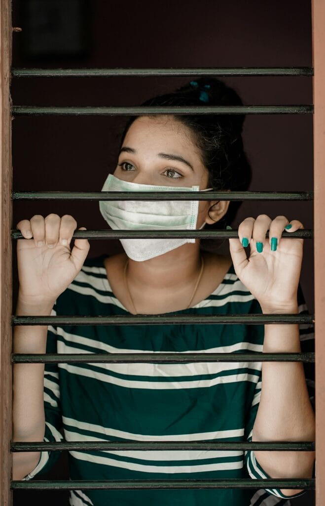 A woman wearing a face mask looks through window bars during COVID-19 lockdown.