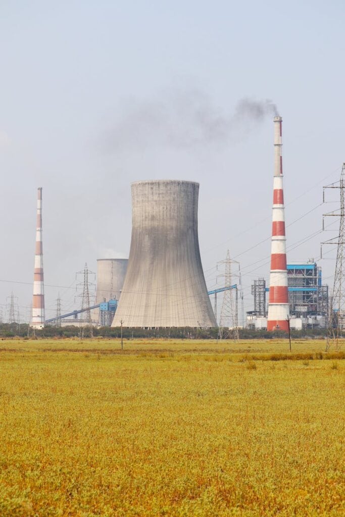 A cooling tower and smokestacks release emissions in a rural field near Vijayawada, India.